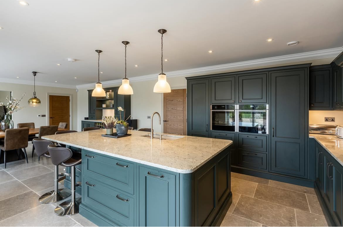 Bespoke blue kitchen-diner with stone worktops, large grey floor tiles and 3 feature glass pendants over the central island
